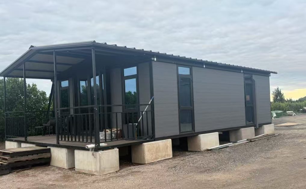 Long grey HuoSheng container house with veranda resting on foundation blocks