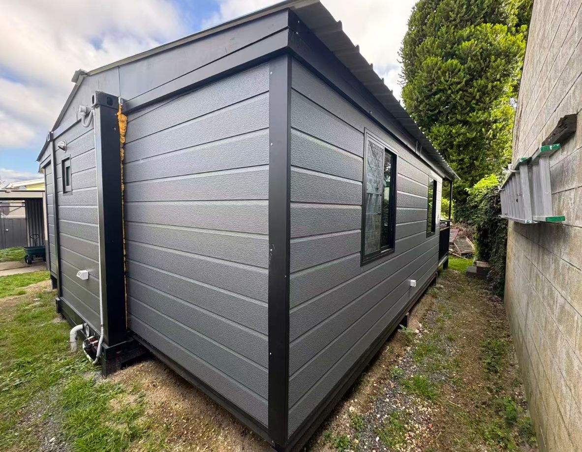 Compact grey HuoSheng container house installed on piles beside a garden wall