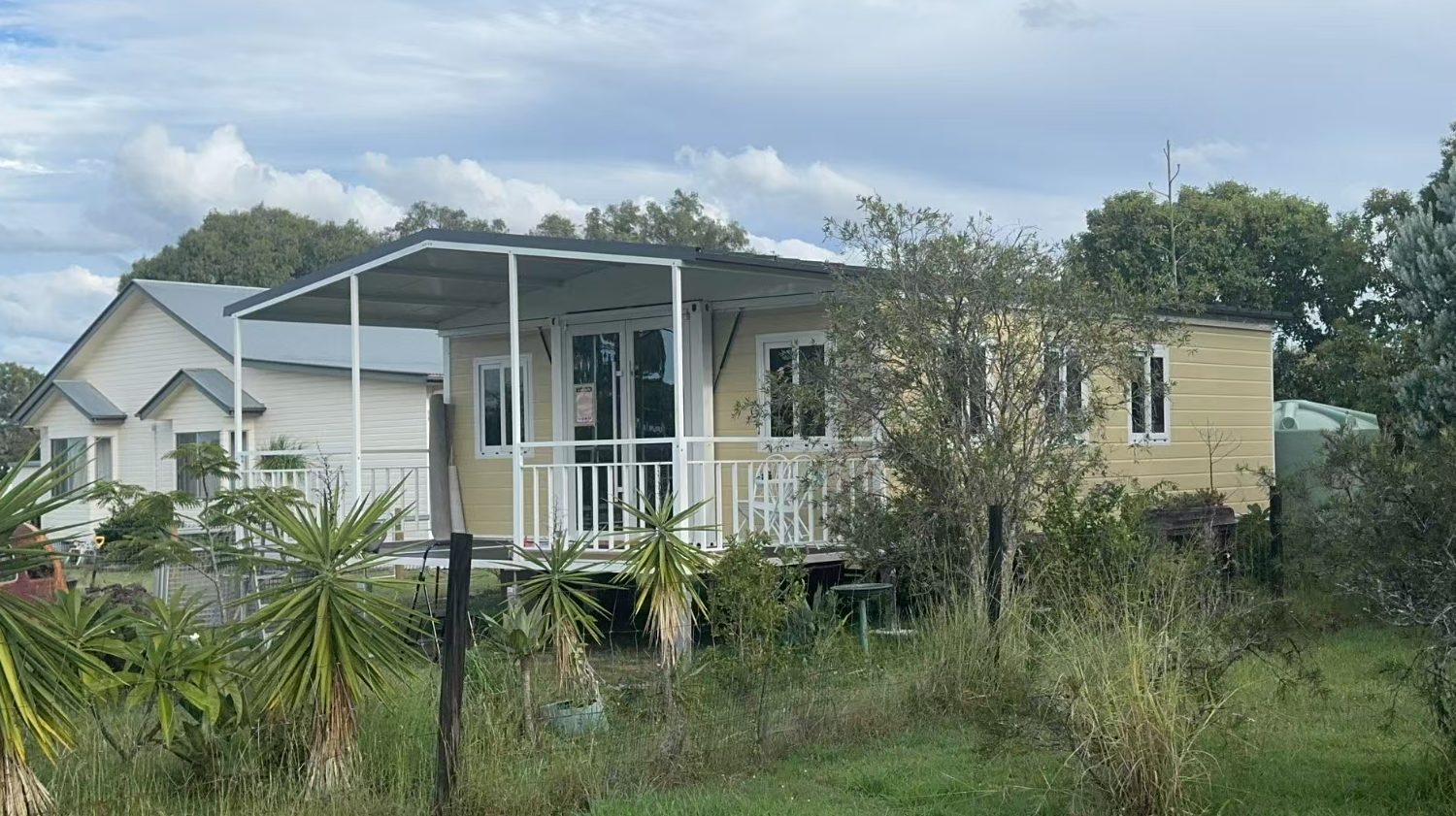 Cream-colored HuoSheng folding house with a white veranda in a garden setting