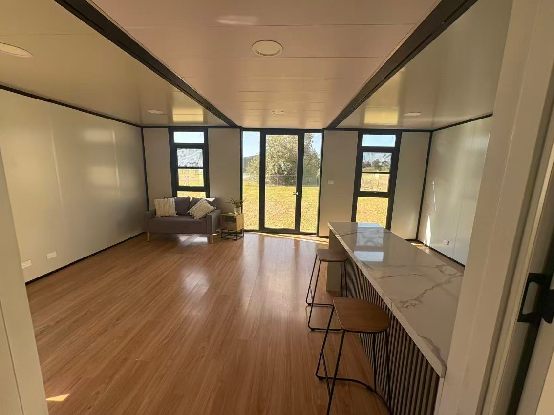 Bright open-plan living room of a HuoSheng expandable container house with timber floor