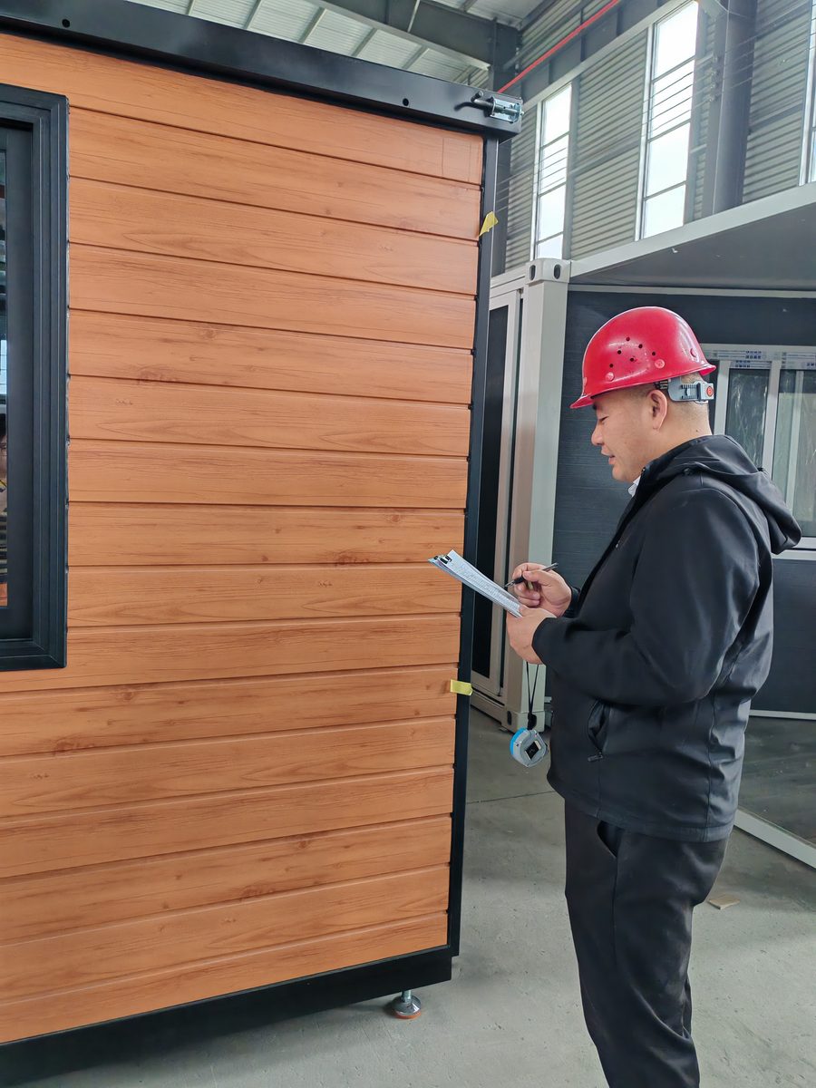 HuoSheng quality inspector checking the wood-grain wall panels of a finished unit